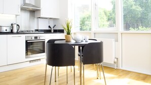 A modern kitchen with white cabinetry, a built-in oven, and a dining table with black chairs. - Shoreditch Apartments (London)