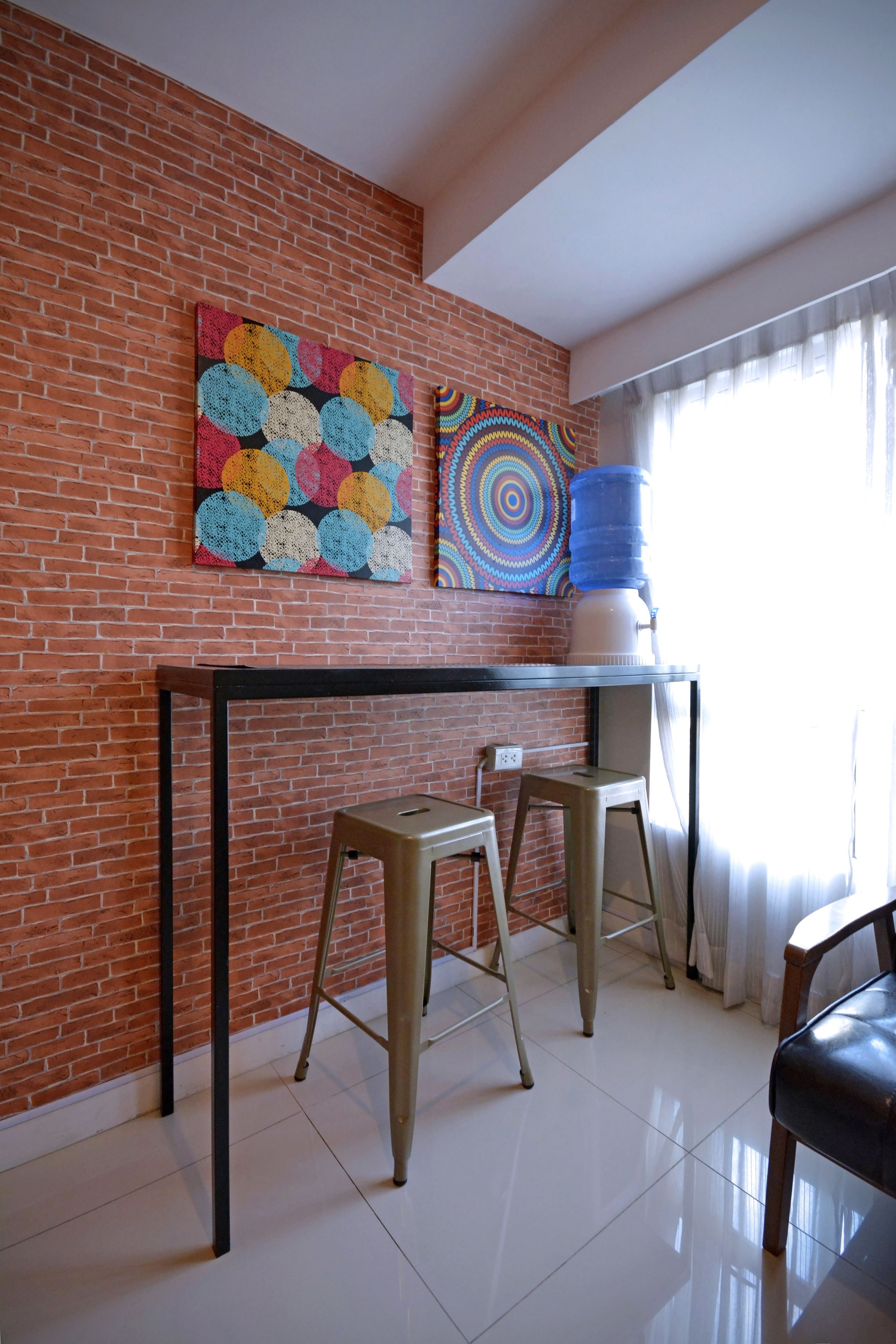 A room with a brick wall, a black table, two stools, and a water dispenser.