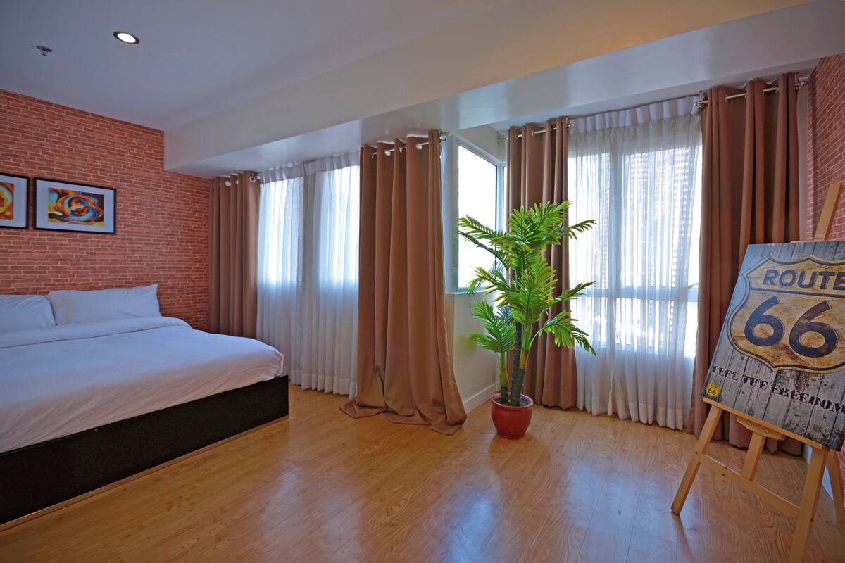 Een hotelkamer met een bed, een bloempot, een Route 66 bord en een bakstenen muur.