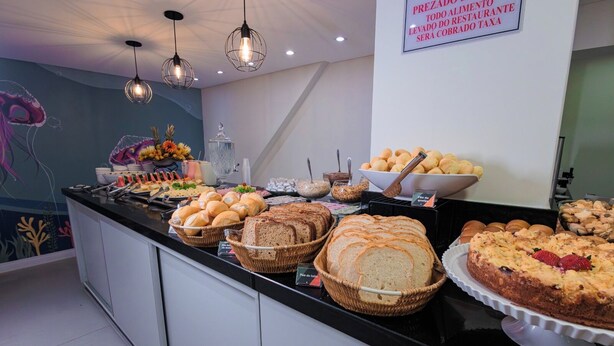 A buffet with various breads, pastries, and a cake. - Sagres Praia Hotel (Balneário Camboriú)