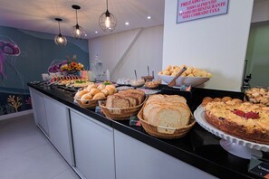 A buffet with various breads, pastries, and a cake. - Sagres Praia Hotel (Balneário Camboriú)
