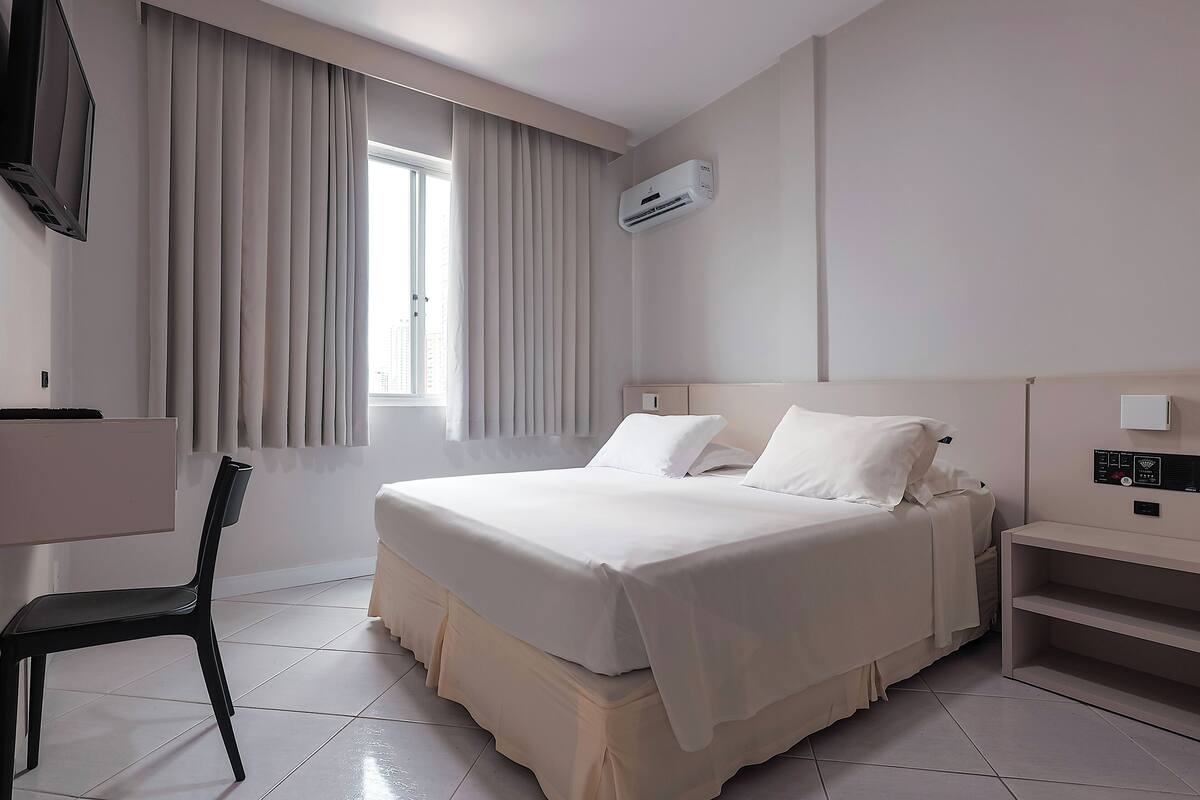 Une chambre d’hôtel moderne avec un grand lit, une chaise, un bureau et une fenêtre avec des rideaux.
