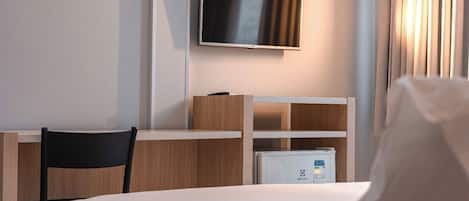 A hotel room with a bed, a desk, a chair, a television, and a minibar.