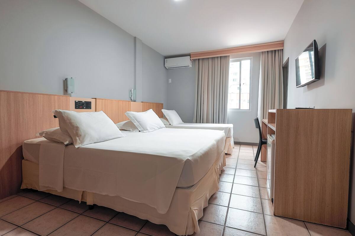 Une chambre d’hôtel avec deux lits, un bureau, une télévision et une armoire.