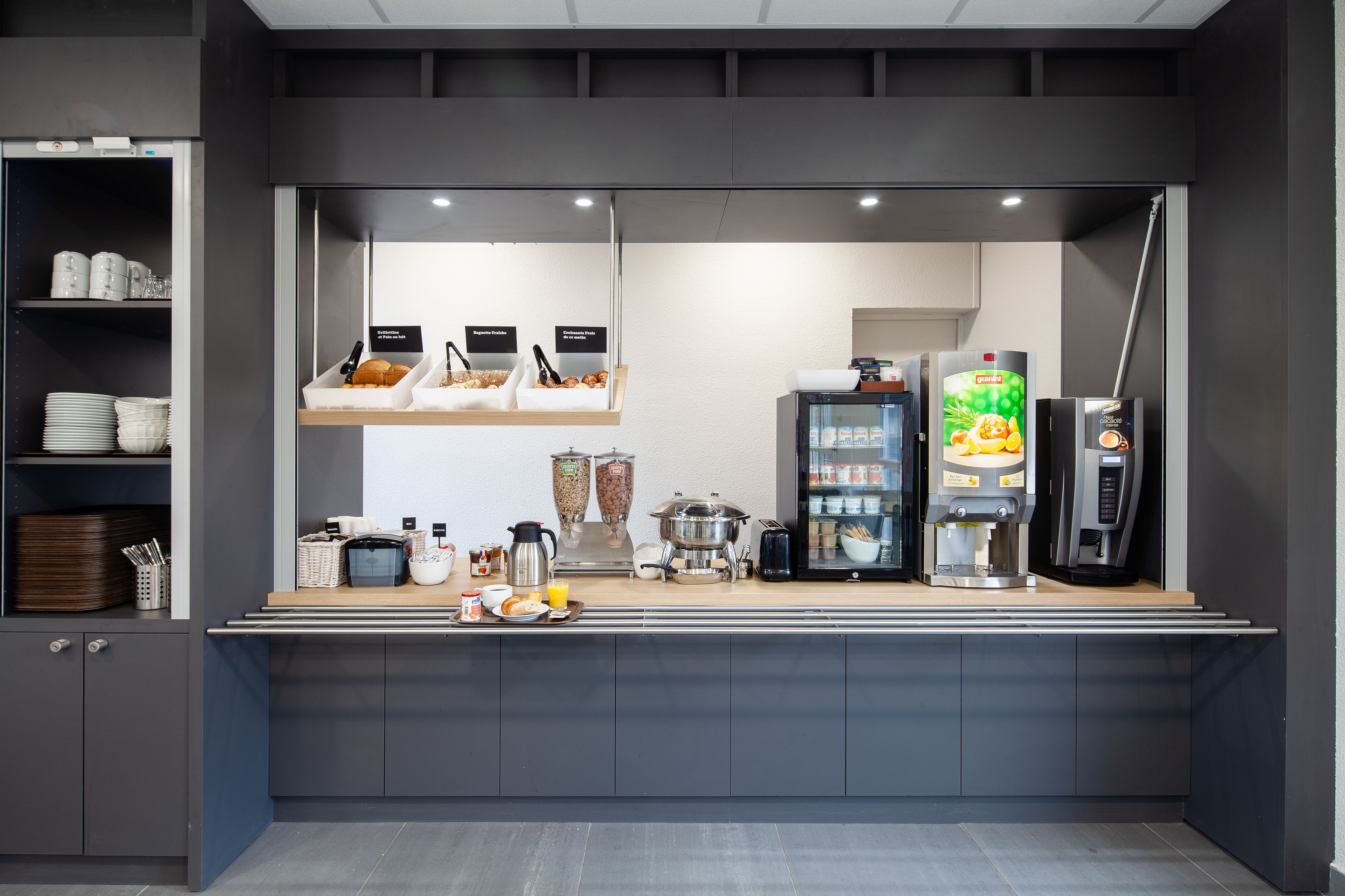 A modern breakfast bar with a coffee machine, a refrigerator, and a variety of food items.