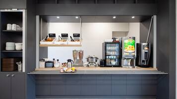 A modern breakfast bar with a coffee machine, a refrigerator, and a variety of food items.