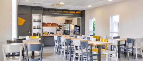 Un café moderno con mostrador, zona de estar y cocina al fondo.