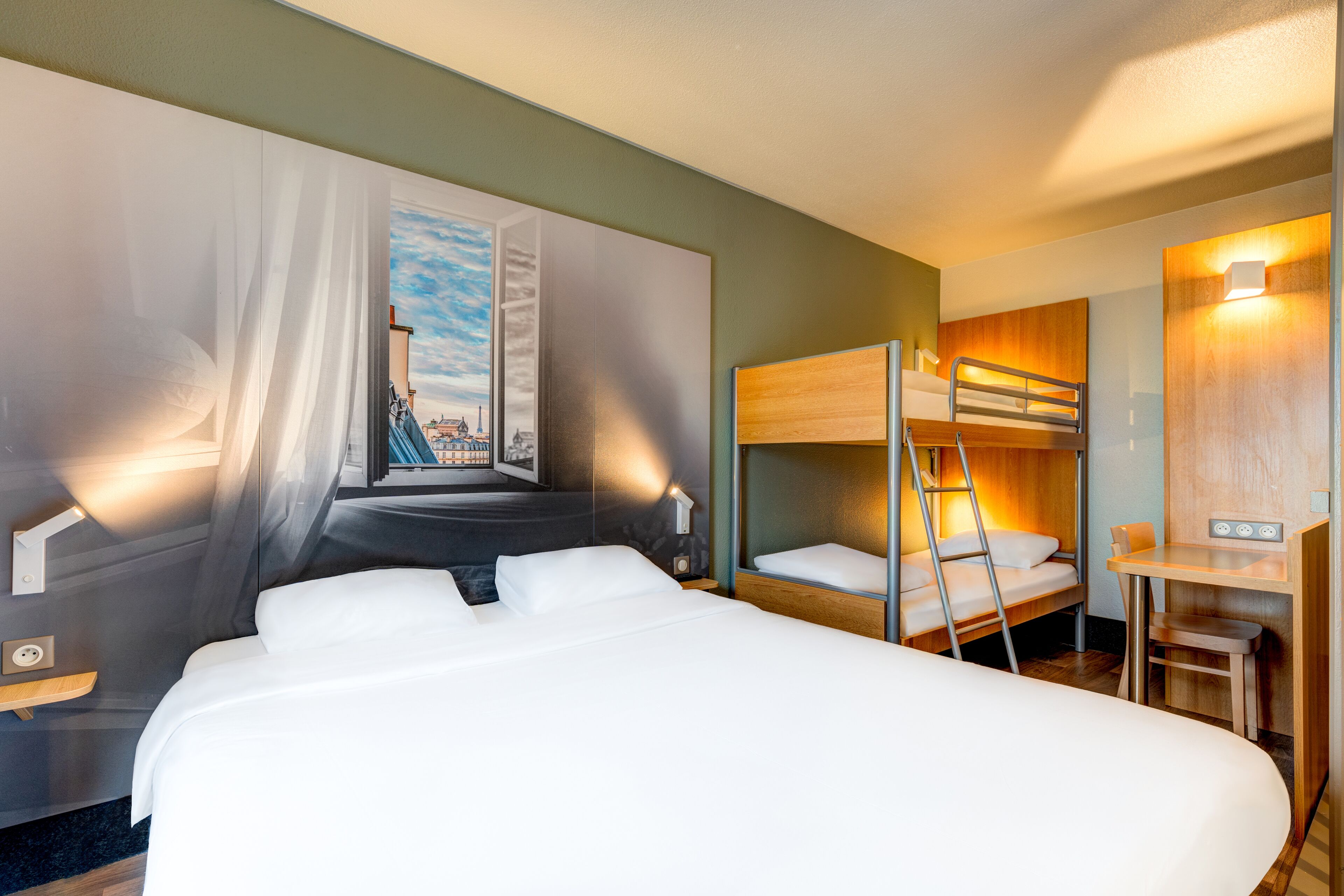 Una habitación de hotel con una cama grande, una litera, un escritorio y una silla.