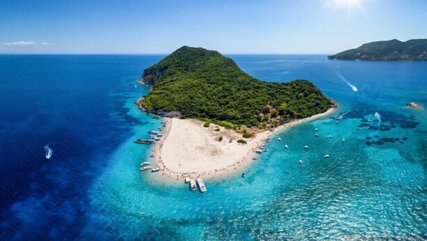 An aerial view of a tropical island with a sandy beach, clear turquoise waters, and boats anchored near the shore. - Blue Lake (Zakynthos)