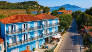 A multi-story hotel with balconies, a paved street, and a view of the sea and hills in the background. - Blue Lake (Zakynthos)