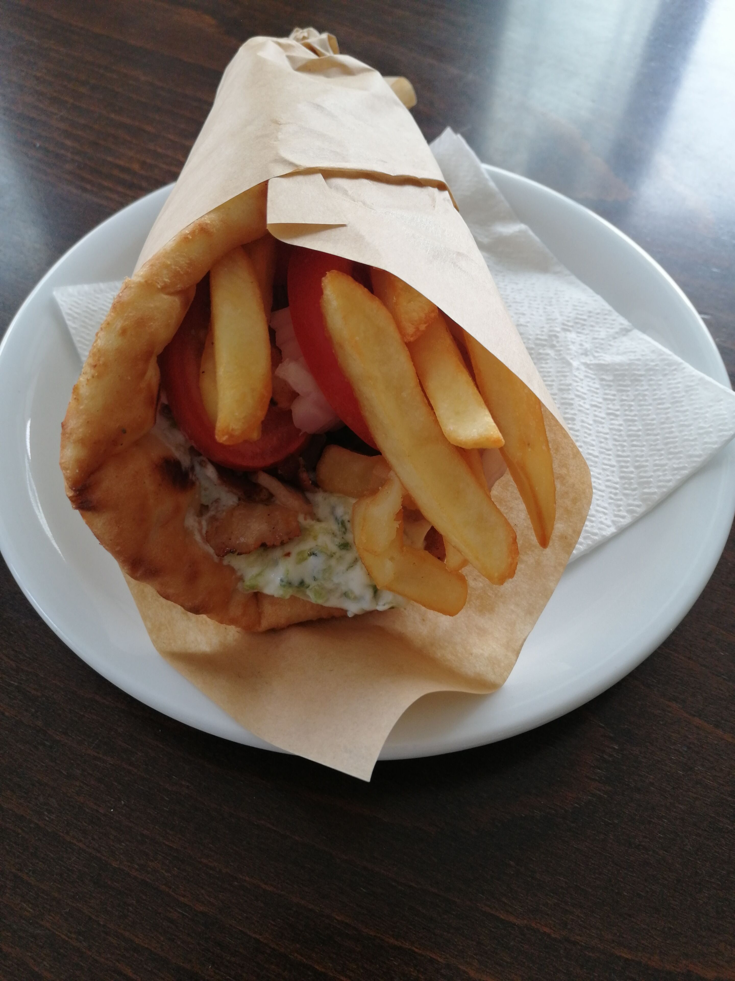 Een wrap belegd met friet en tomaat op een wit bord.
