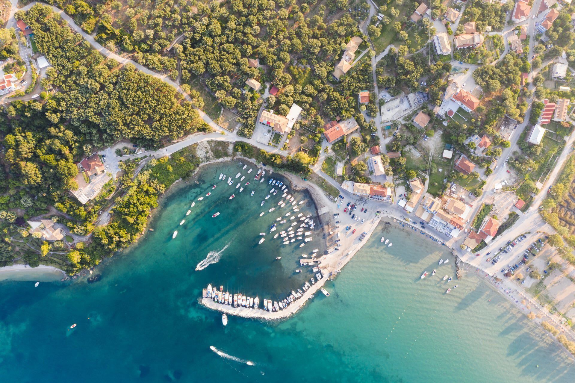 Vue aérienne d’une zone côtière avec un port de plaisance, des bâtiments et une route.
