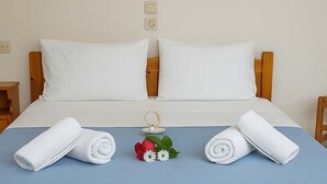 A neatly made bed with white linens, two rolled towels, and a small floral arrangement on a blue bedspread. - Blue Lake (Zakynthos)