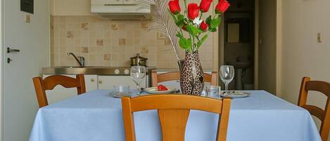 Un comedor con una mesa dispuesta para dos, un florero con rosas rojas y una cocina al fondo.