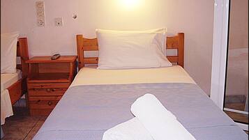 Un letto singolo con cuscino e coperta bianchi, un comodino in legno con un telecomando e una presa elettrica.