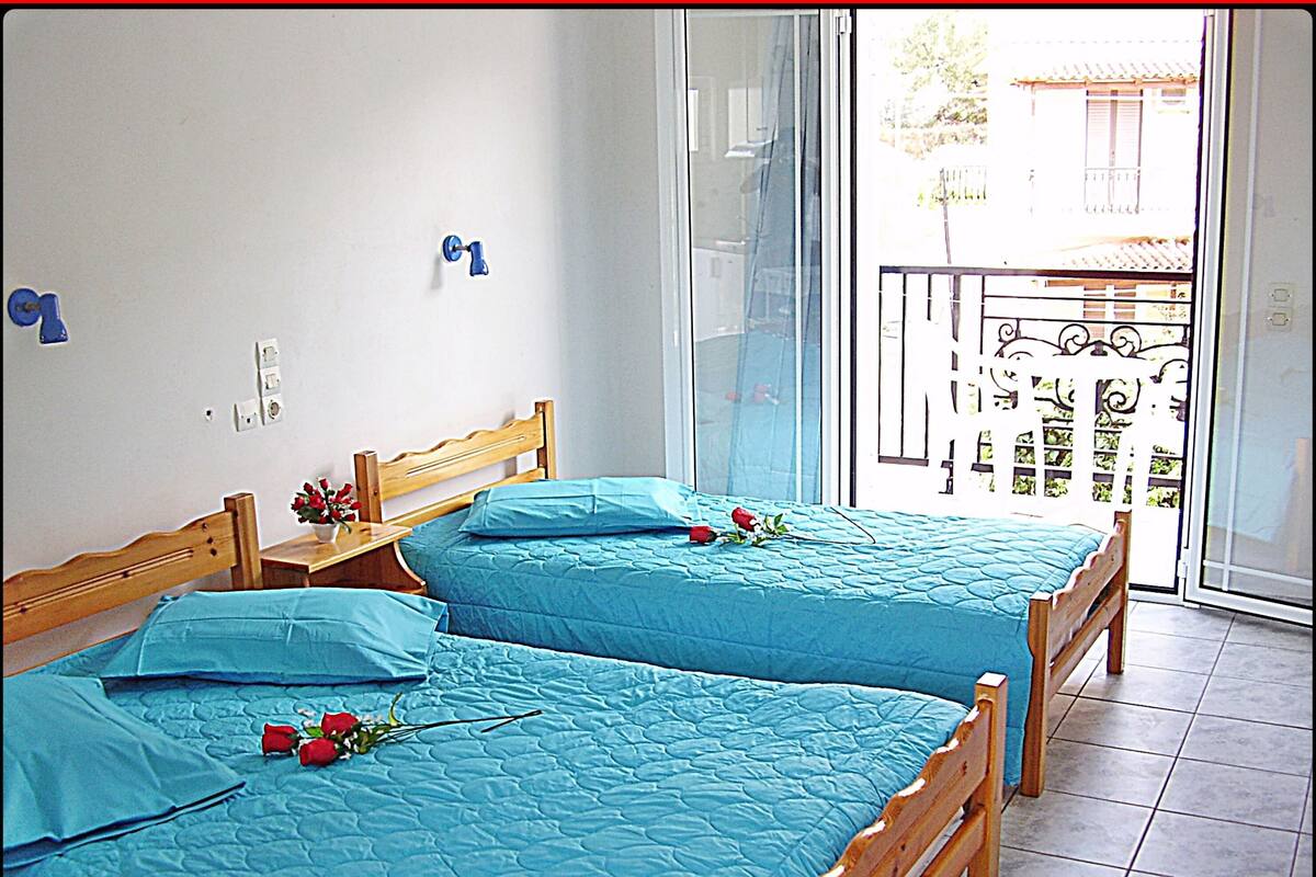 Ein Zimmer mit zwei Holzbetten, jedes mit einer blauen Steude und einer einzelnen roten Rose.