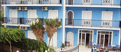 A two-story building with balconies, air conditioning units, and a stone wall with potted plants.