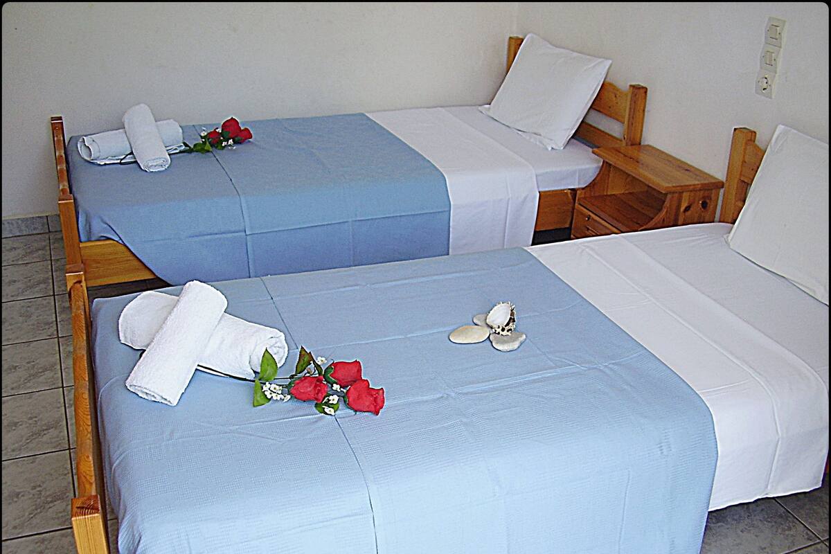 Zwei Einzelbetten mit blau-weißer Bettwäsche, jedes mit einem gerollten weißen Handtuch und einer roten Rose.