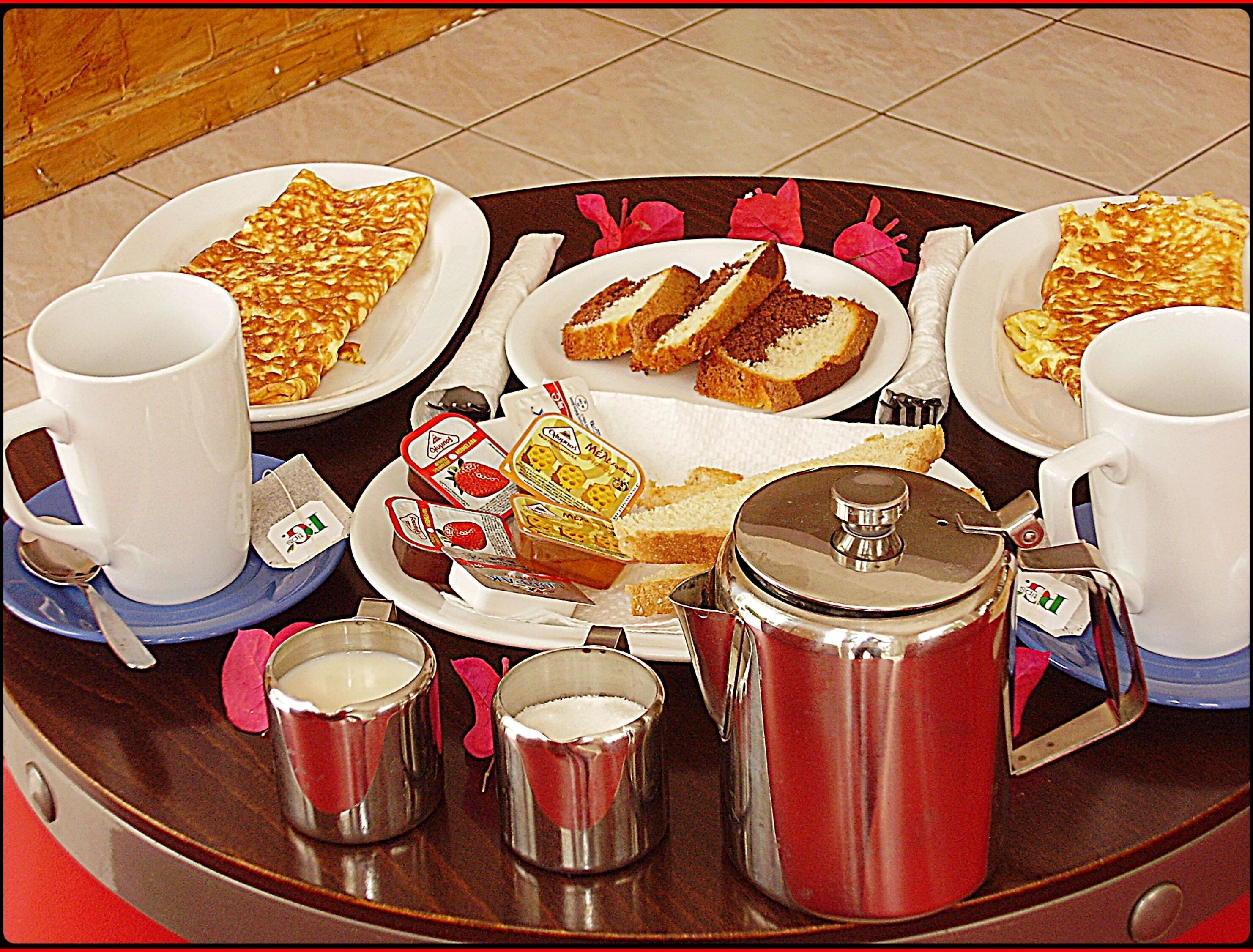 Una mesa de desayuno con platos de comida, tazas y una cafetera.