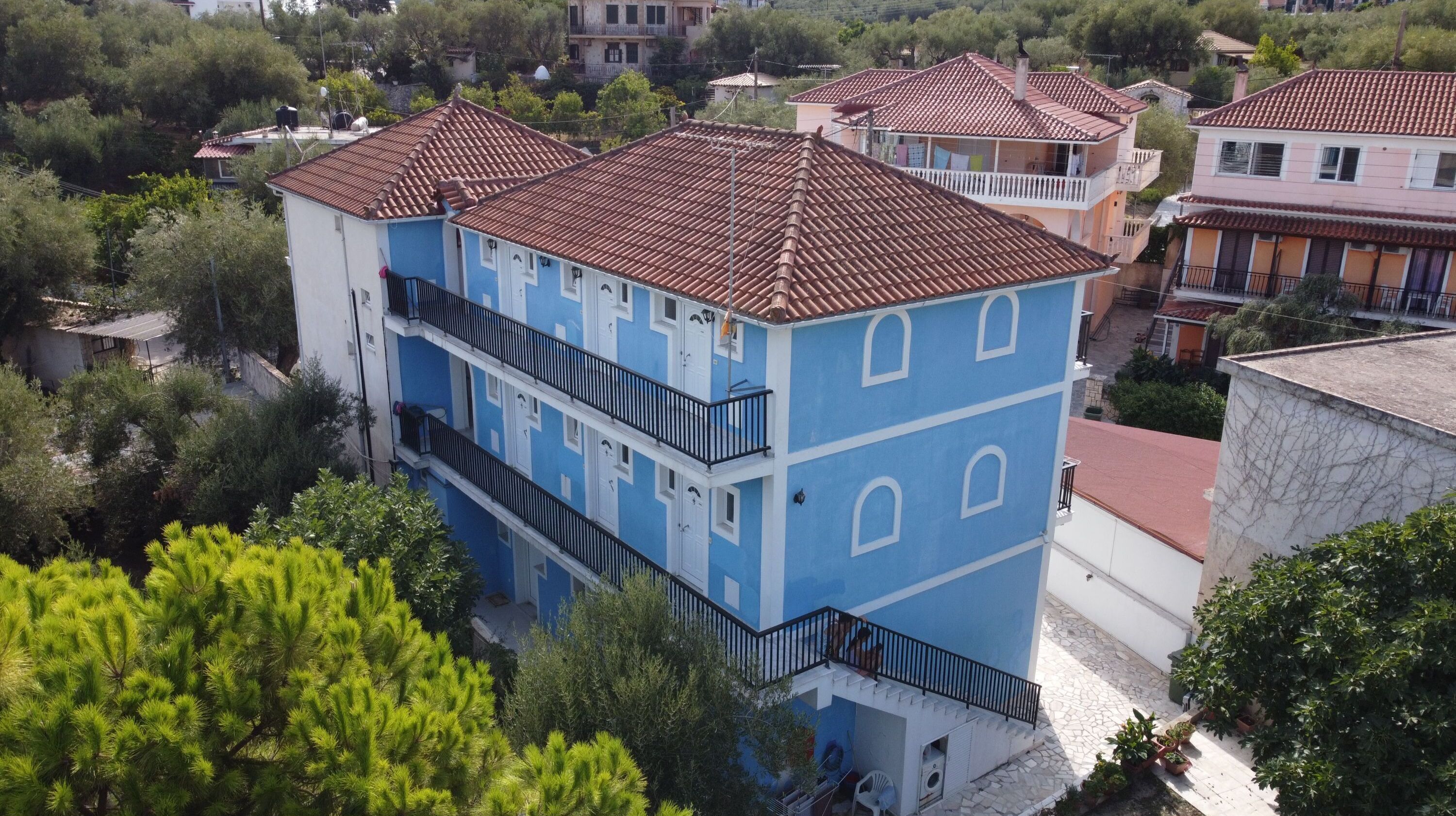 A multi-story building with a tiled roof, balconies, and a mix of vegetation around.