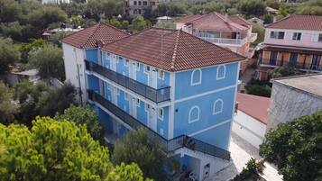 Un edificio de varios pisos con techo de tejas, balcones y una variedad de vegetación alrededor.