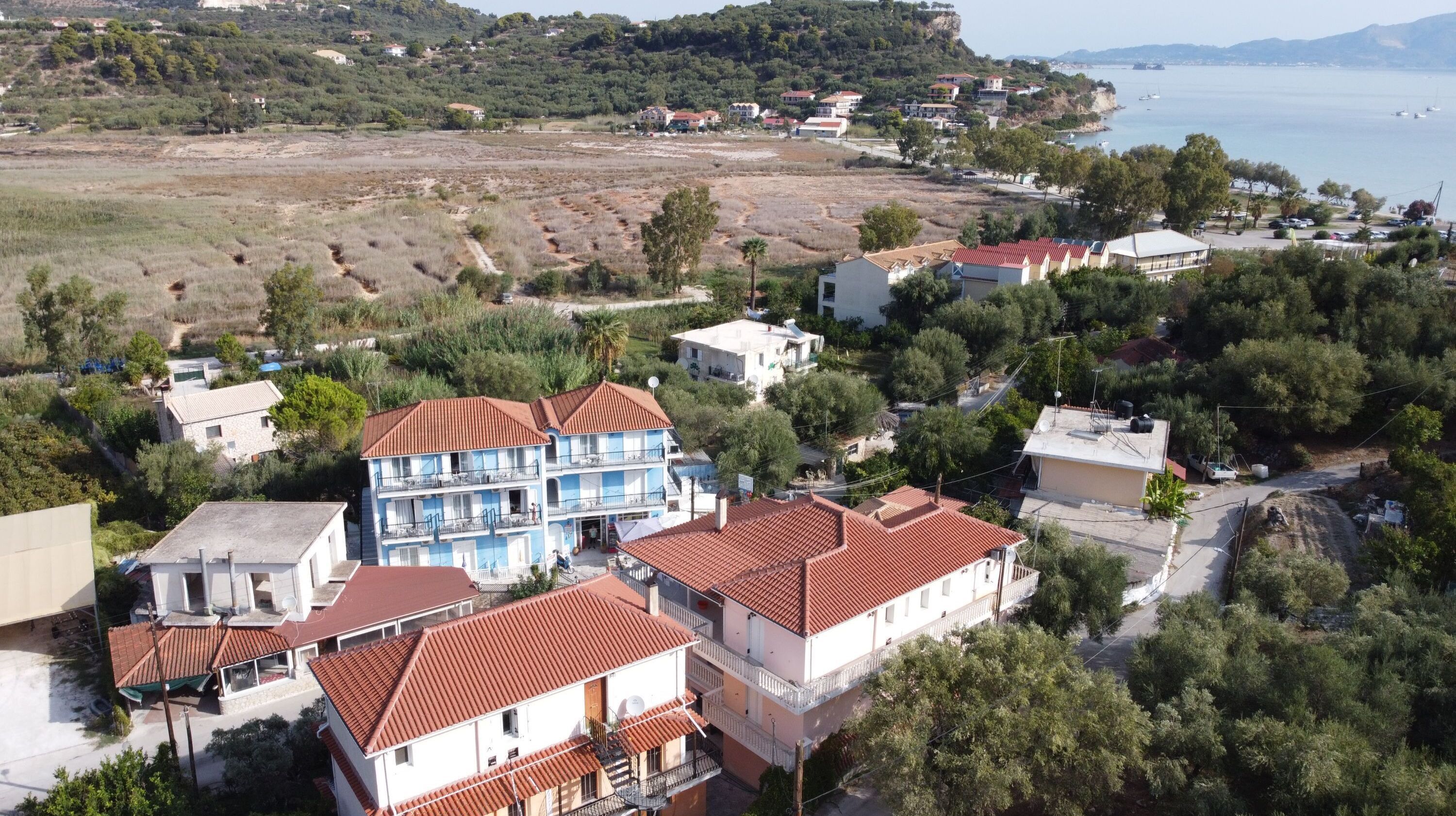 Ein Küstenwohngebiet mit Häusern, deren Dächer mit roten Ziegeln gedeckt und mit Balkonen versehen sind, umgeben von Grün und mit Blick auf das Meer.