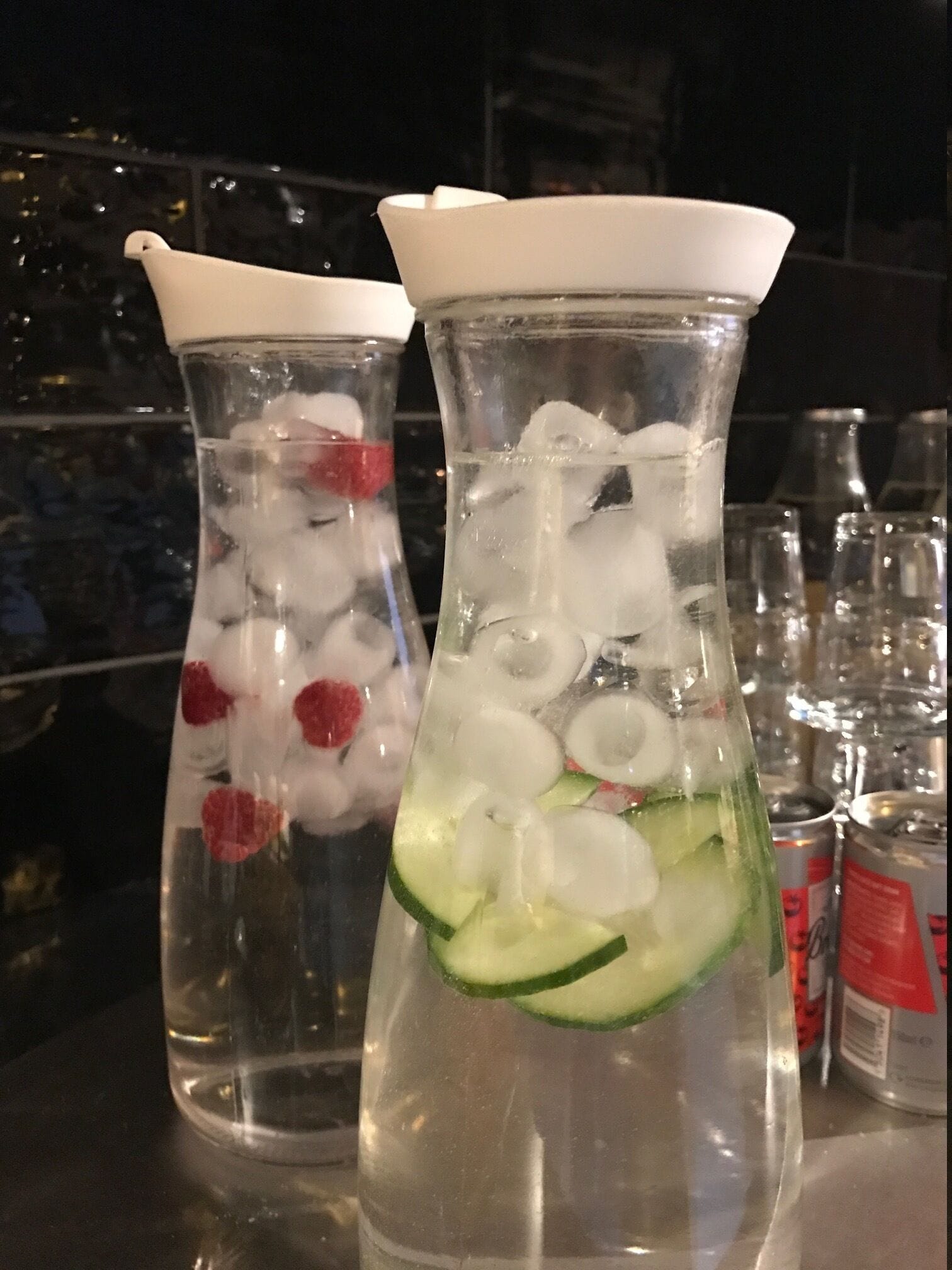 Two clear glass bottles with ice and fruit slices, likely containing beverages, on a bar counter.