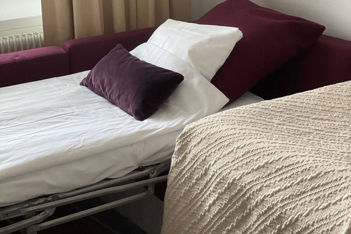 A hotel room with a bed, a window with curtains, and a view of buildings outside.