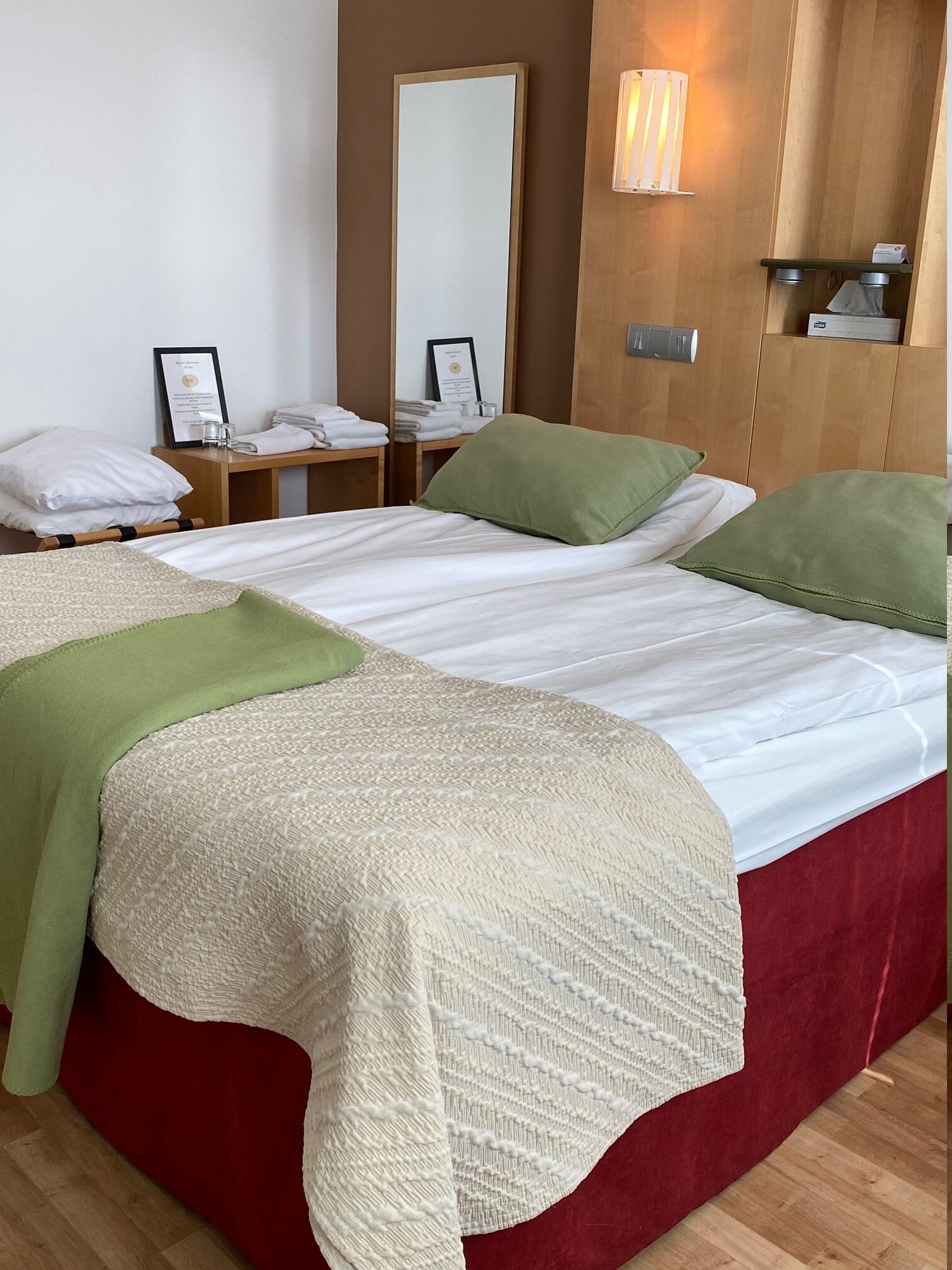 A hotel room with a large bed, a bedside table with a lamp, a mirror, and neatly folded towels.