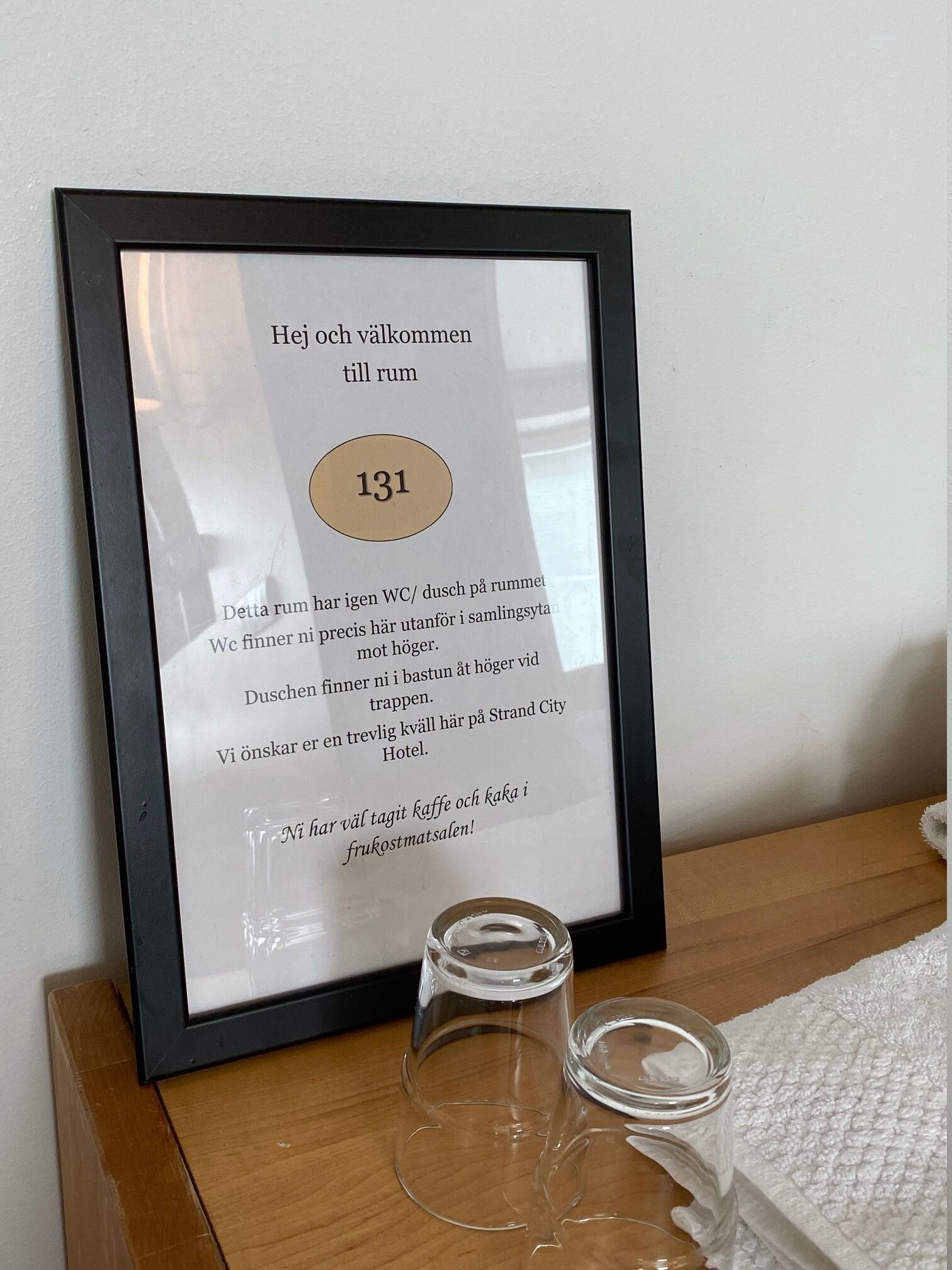A framed sign with text in a foreign language, a number '131', and two empty glasses on a wooden surface.