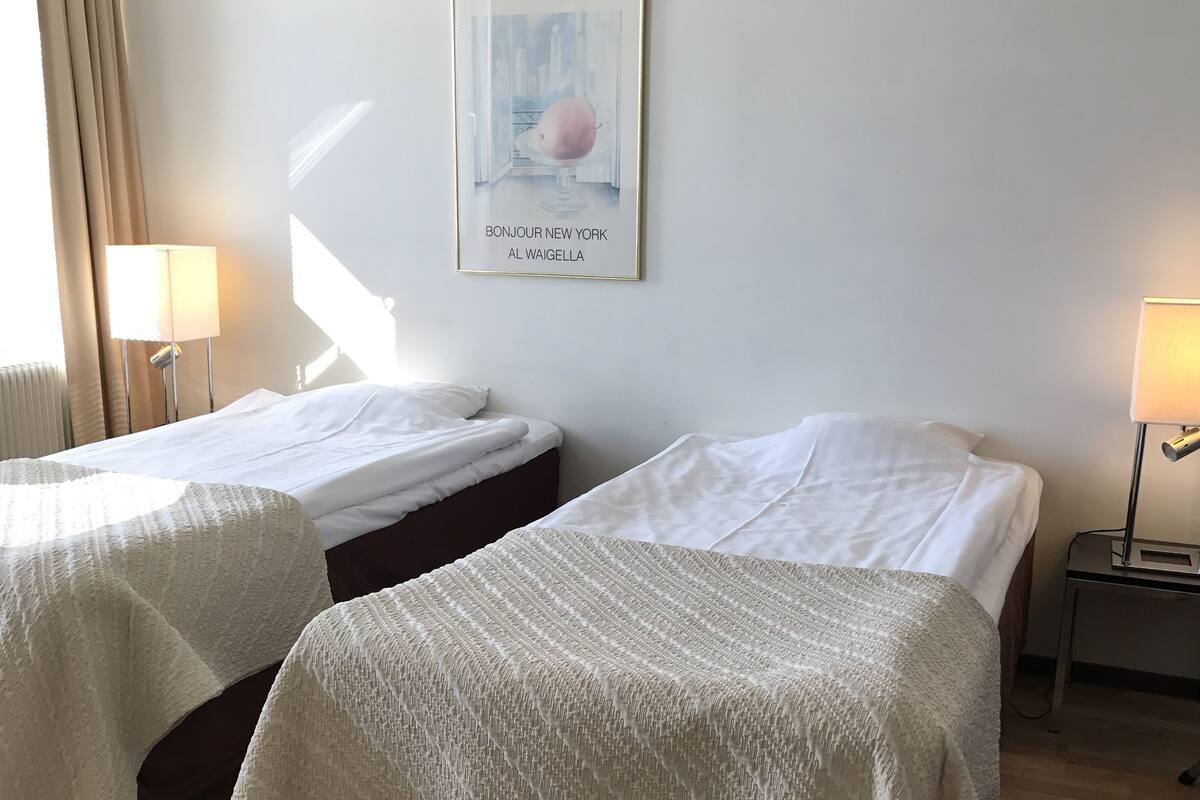 A hotel room with two beds, a framed welcome sign, and a lamp on a bedside table.