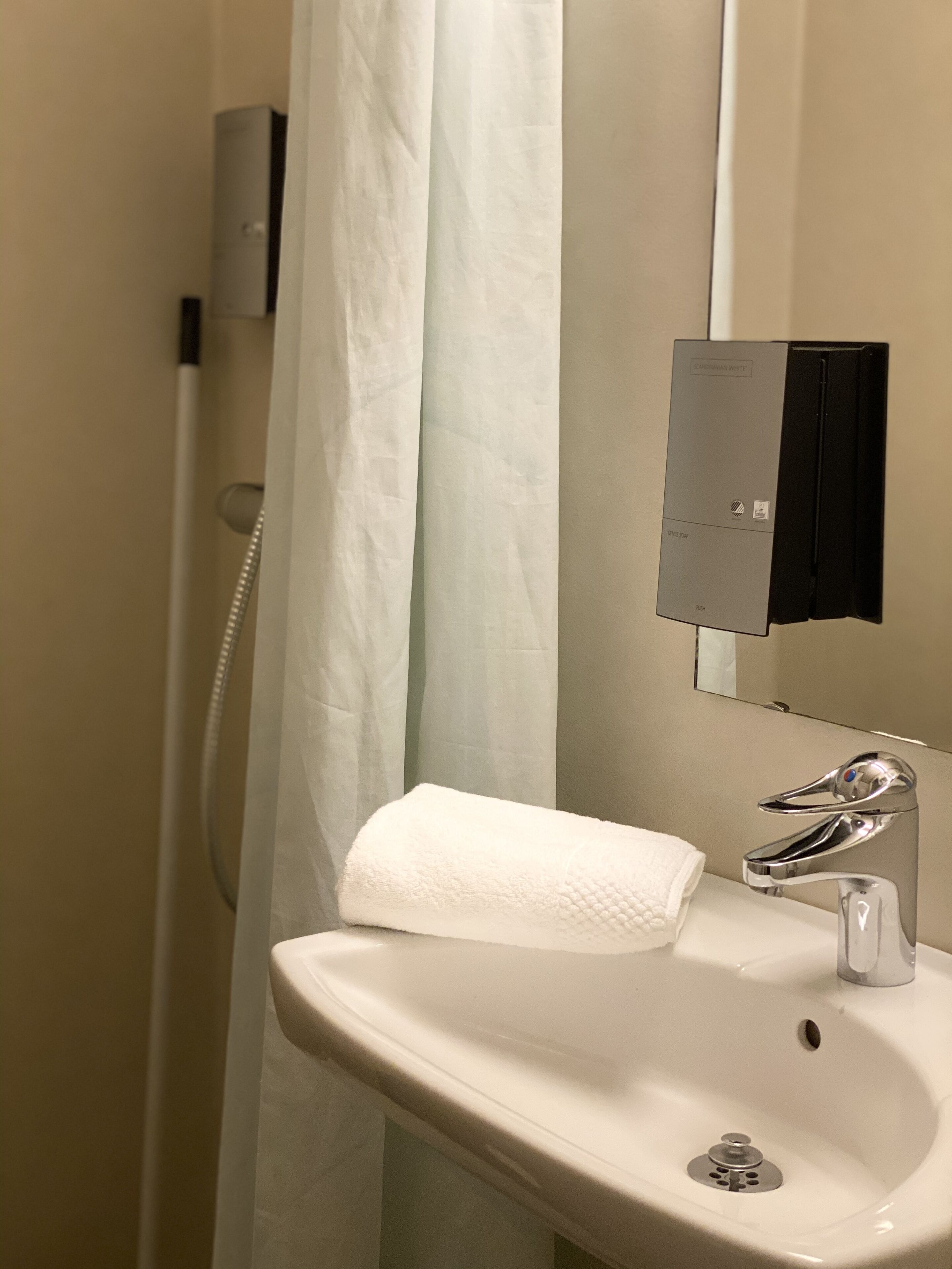 A bathroom with a white sink, a mirror, a shower curtain, and a towel.