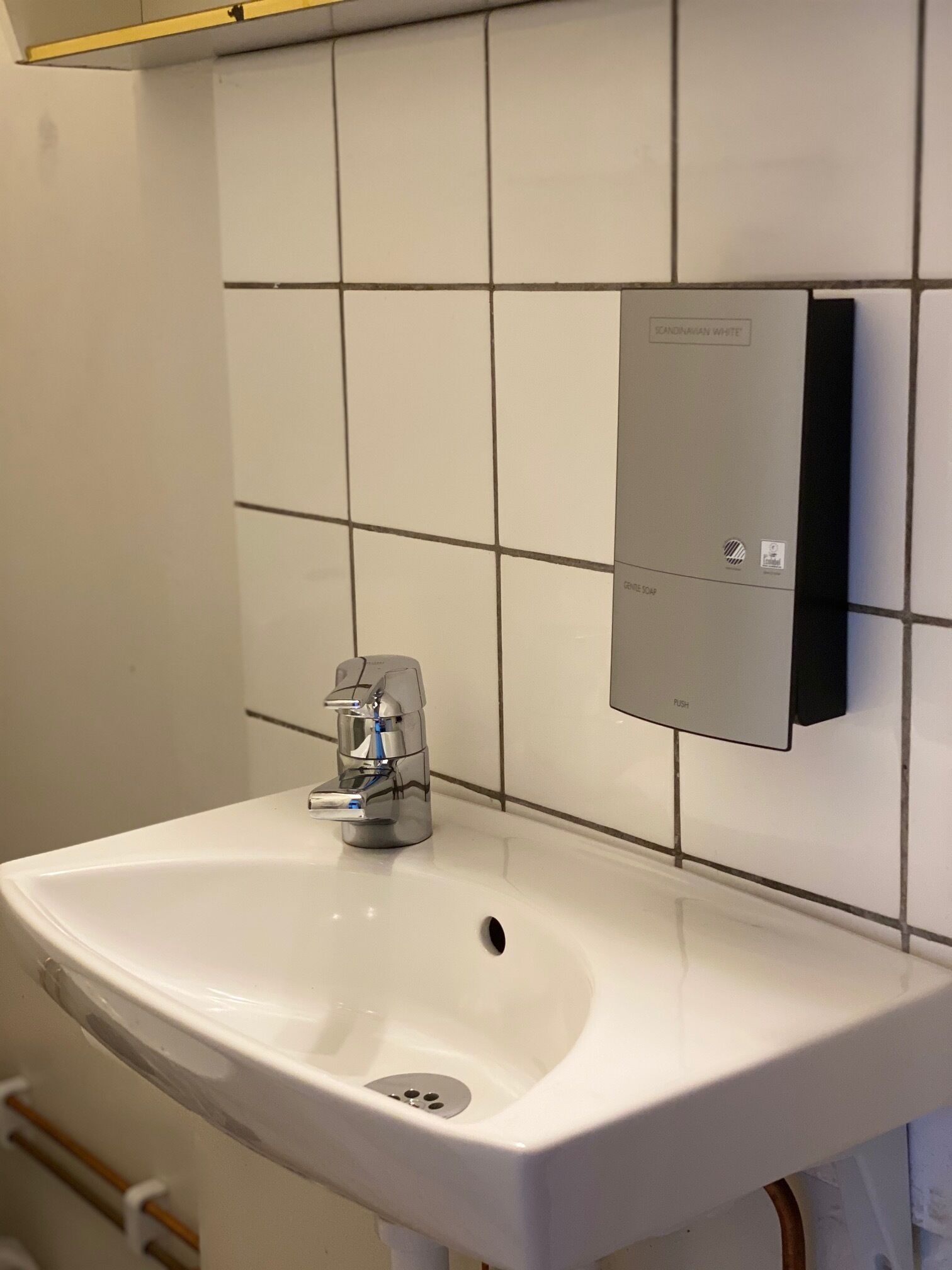 A bathroom with a white sink, a modern faucet, and a soap dispenser mounted on the wall.