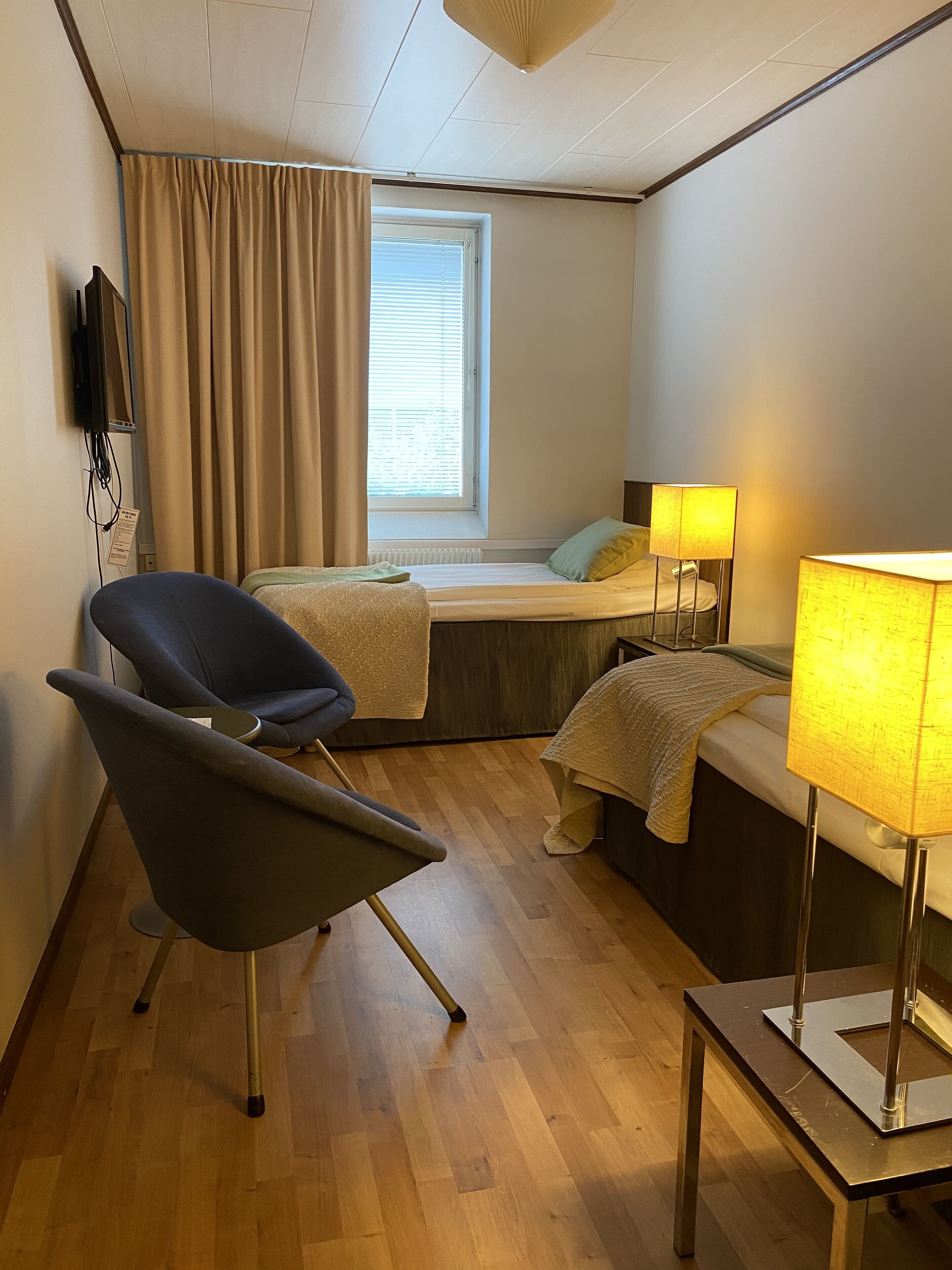Une chambre d’hôtel de taille réduite, comprenant un lit, une chaise, un bureau et une fenêtre avec des rideaux.