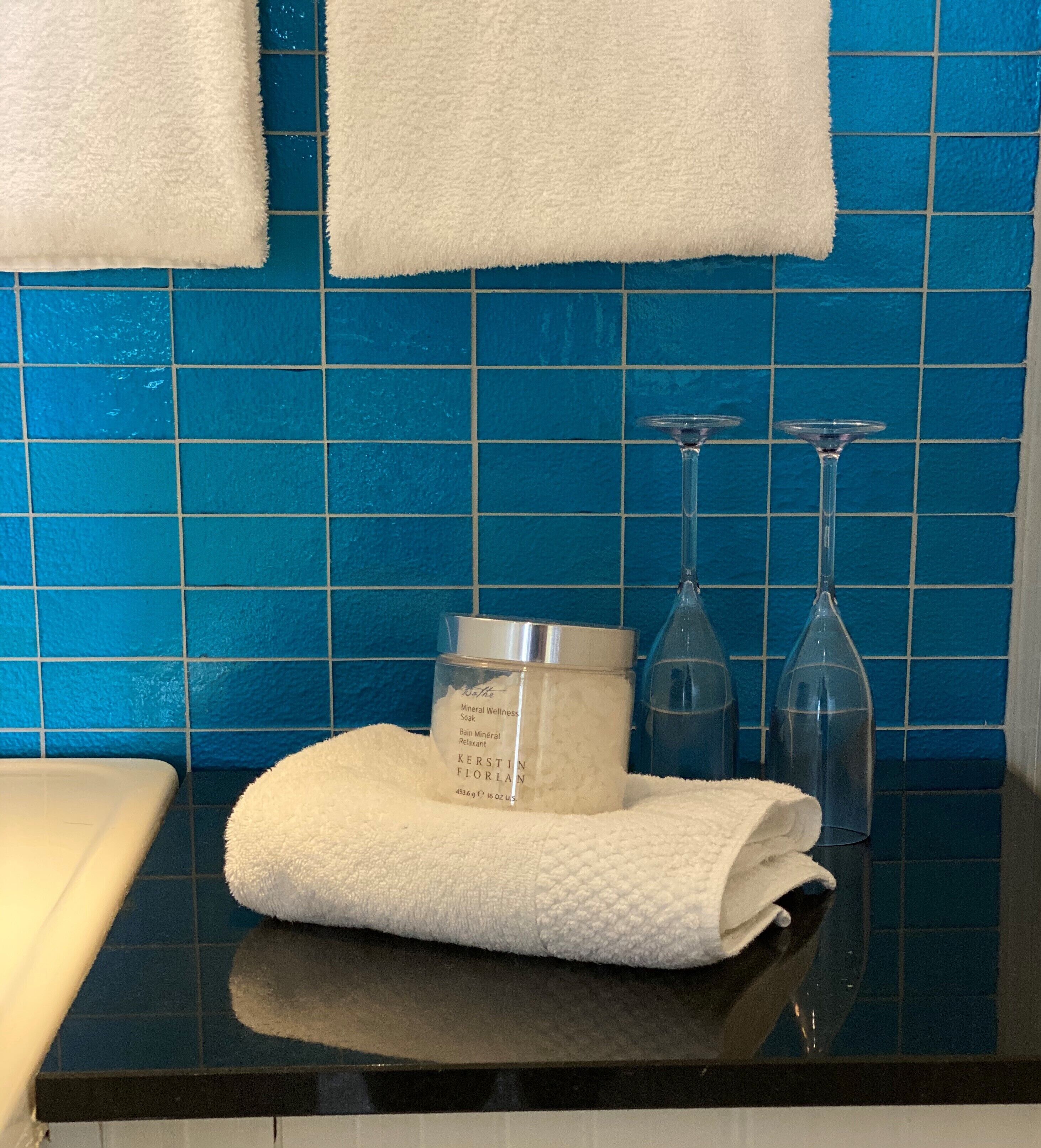 Ett badrum med blå kakelplattor, en vit handduk och en flaska med mineralberikat badsalt.