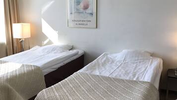 A hotel room with two beds, a framed picture on the wall, and a lamp by the window.