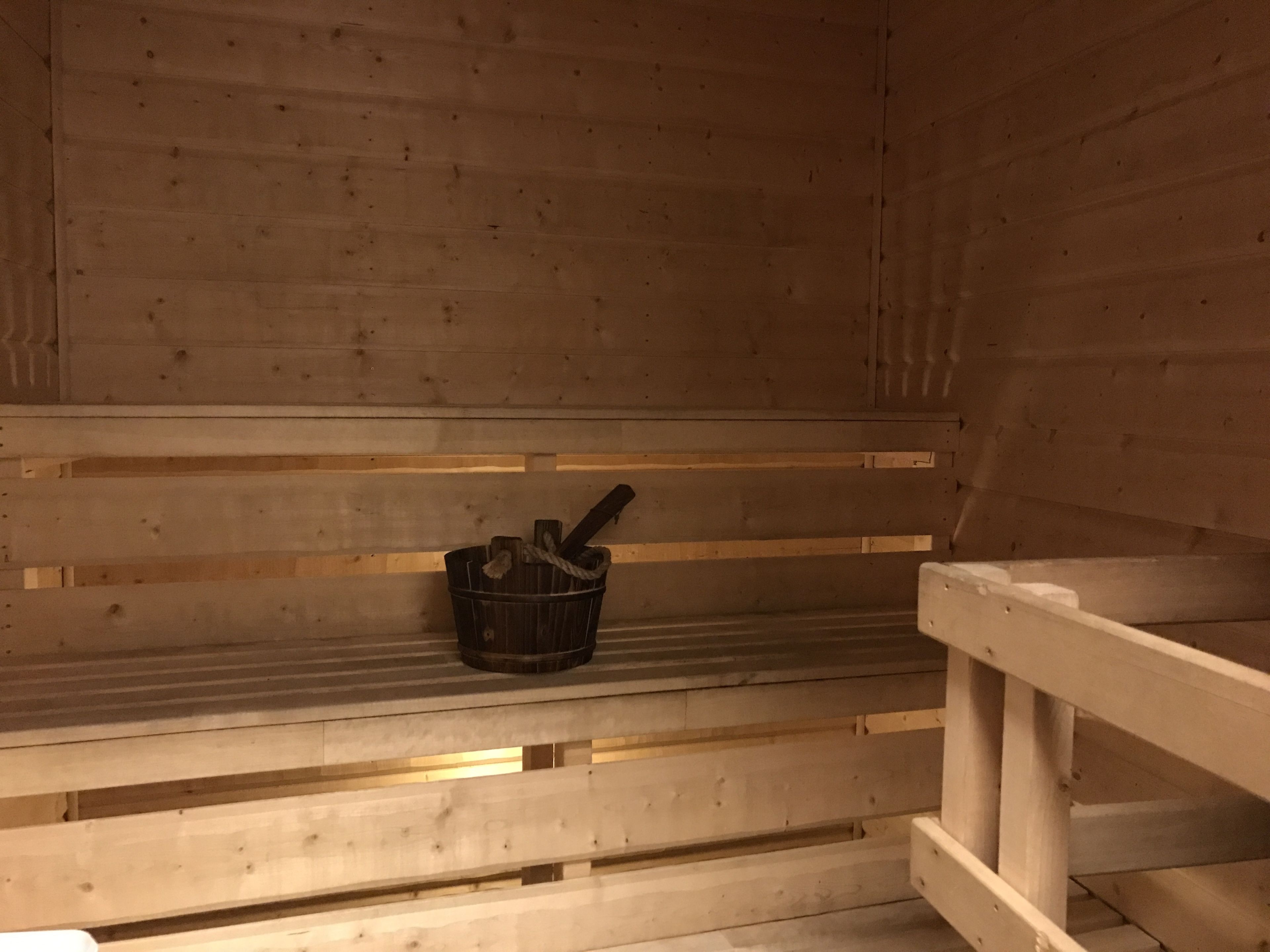 A sauna with wooden benches and a metal bucket.