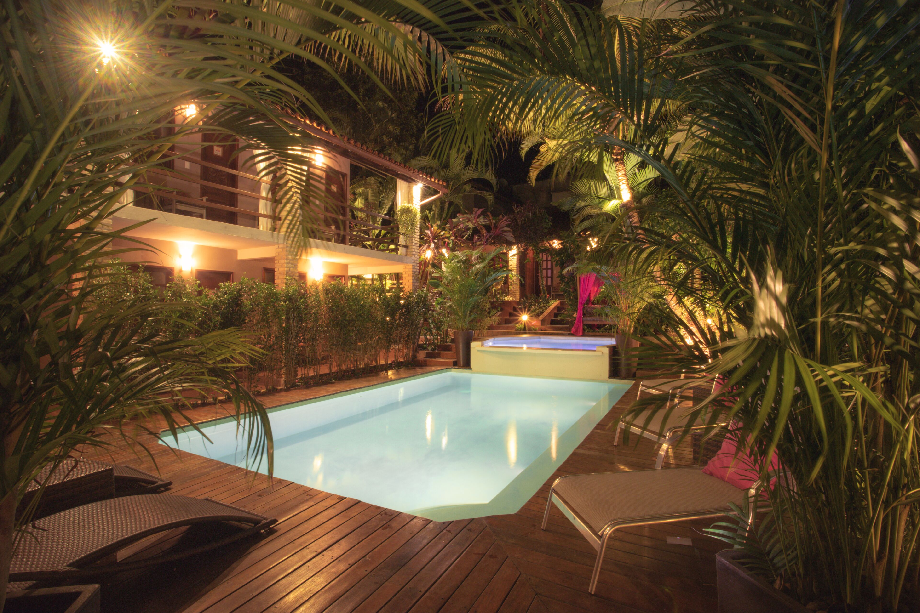A swimming pool surrounded by lush greenery and wooden deck chairs.