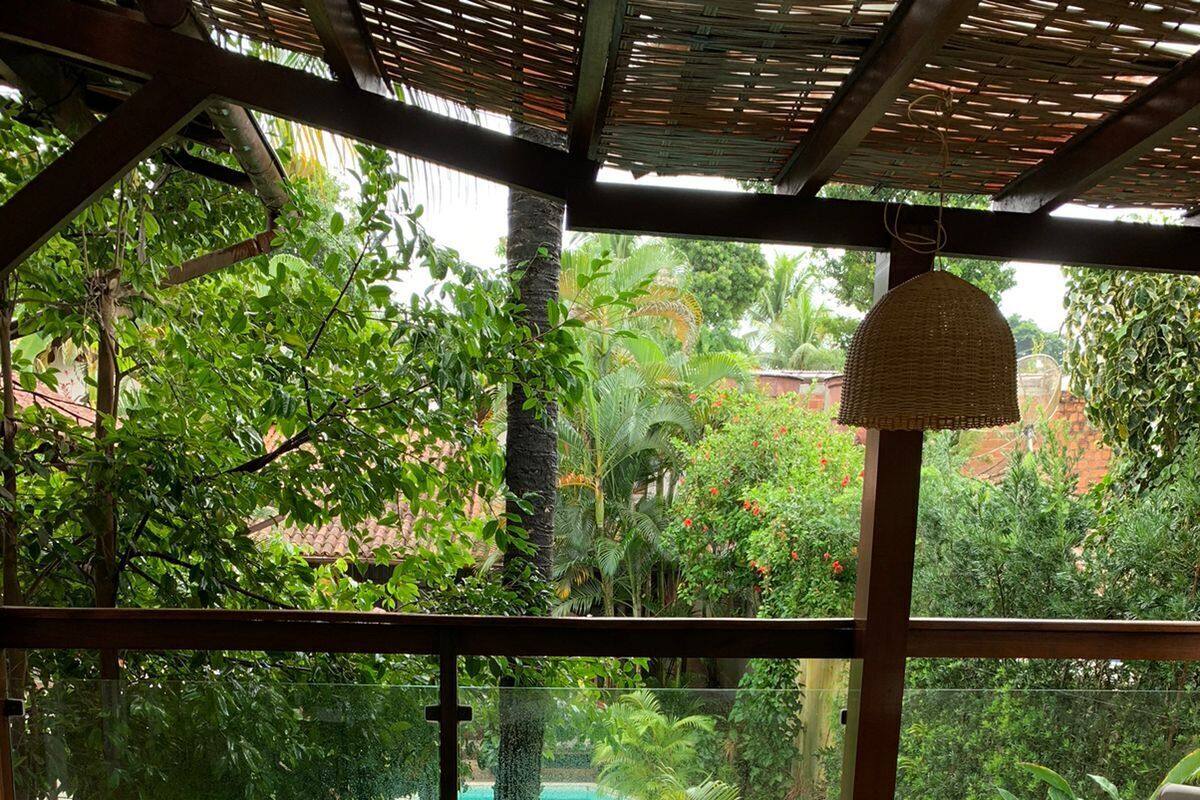 A covered outdoor seating area with wicker furniture, a view of a swimming pool, and lush greenery.