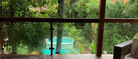A covered outdoor seating area with wicker furniture, a view of a swimming pool, and lush greenery.