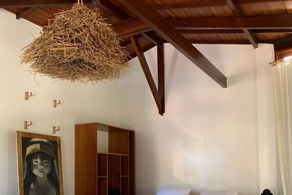 A bedroom with a bed, a wooden wardrobe, a mirror, a hanging light fixture, and a small table.