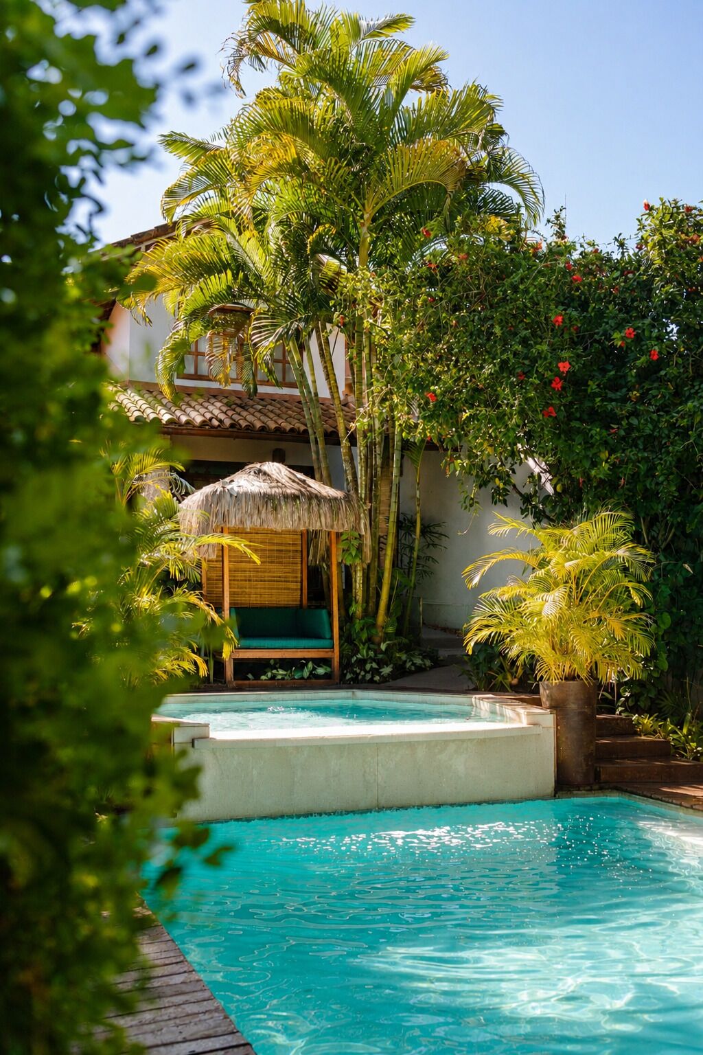 Ein Pool, umgeben von üppiger Vegetation, ein Gebäude mit einem Reetdach und ein Bauwerk mit Ziegeldach.