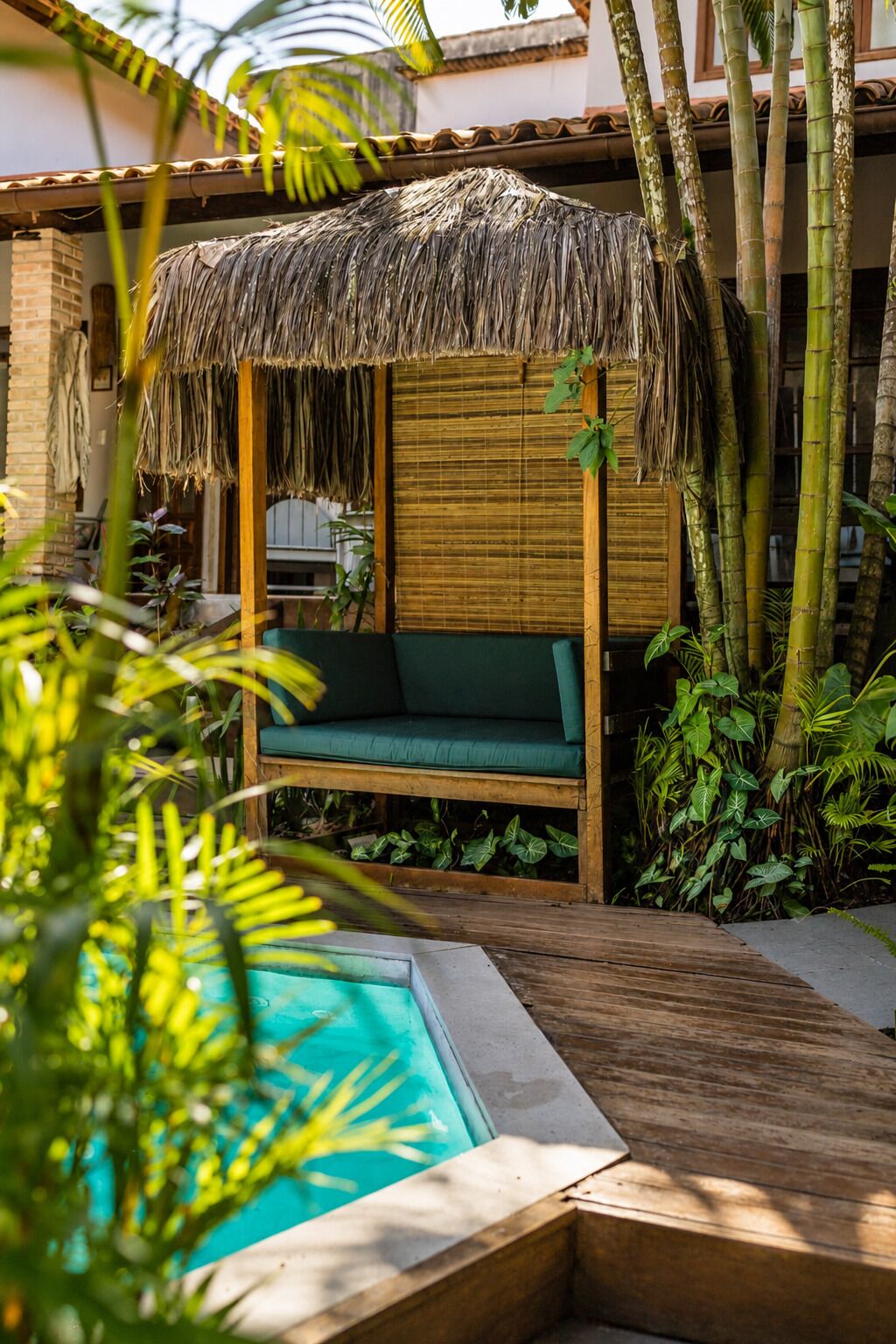 A poolside area with a thatched roof seating area, bamboo plants, and a wooden deck.
