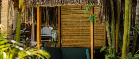 A poolside area with a thatched roof seating area, bamboo plants, and a wooden deck.