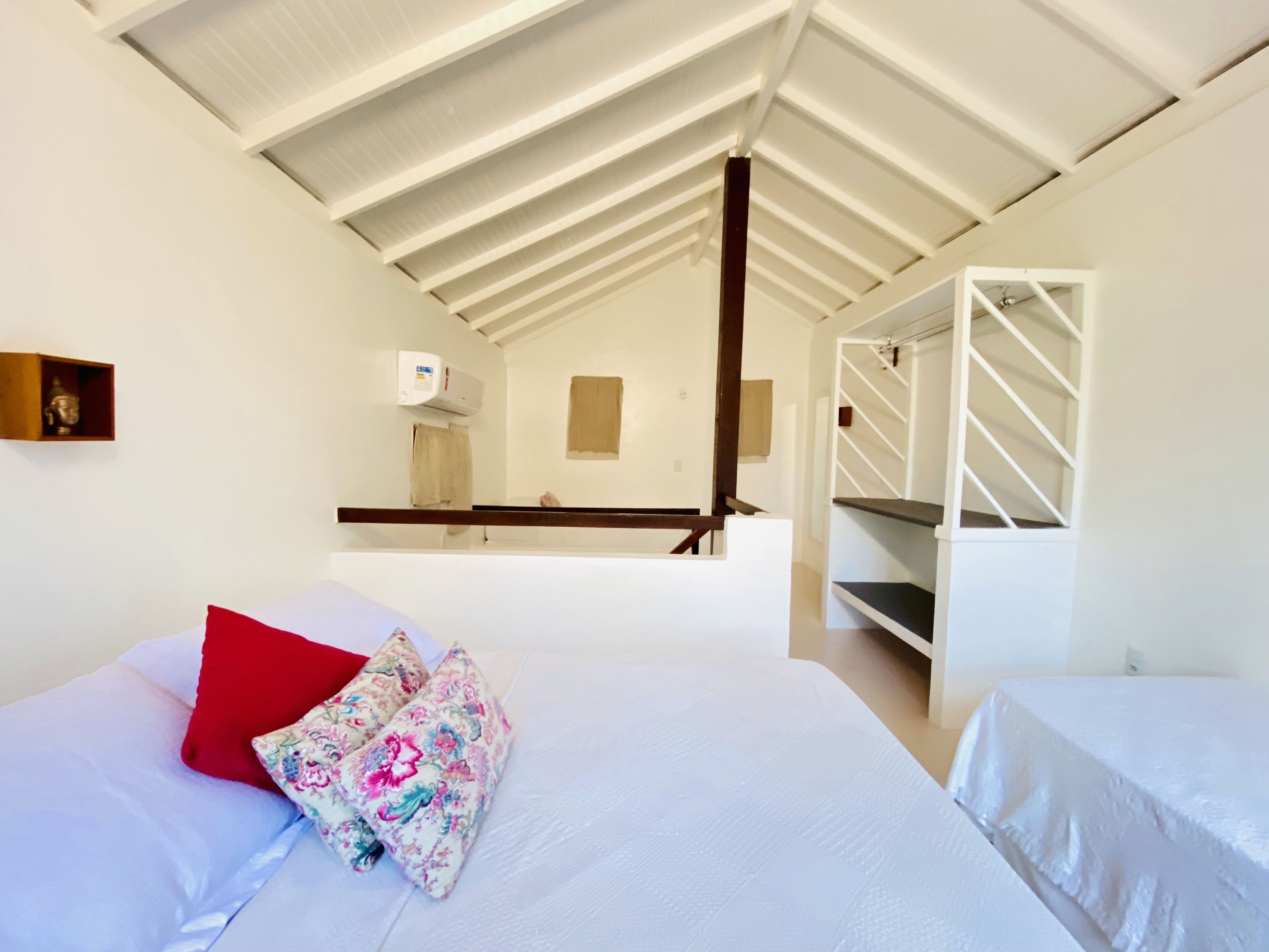 Une chambre à coucher avec un lit, un oreiller rouge, un oreiller à motifs floraux, un couvre-lit blanc et un plafond blanc.