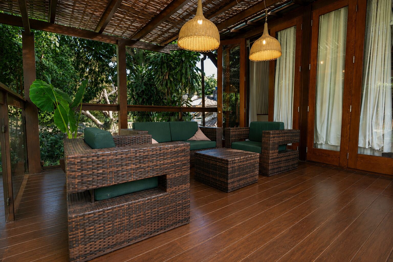 A covered outdoor seating area with wicker furniture, wooden flooring, and hanging lights.