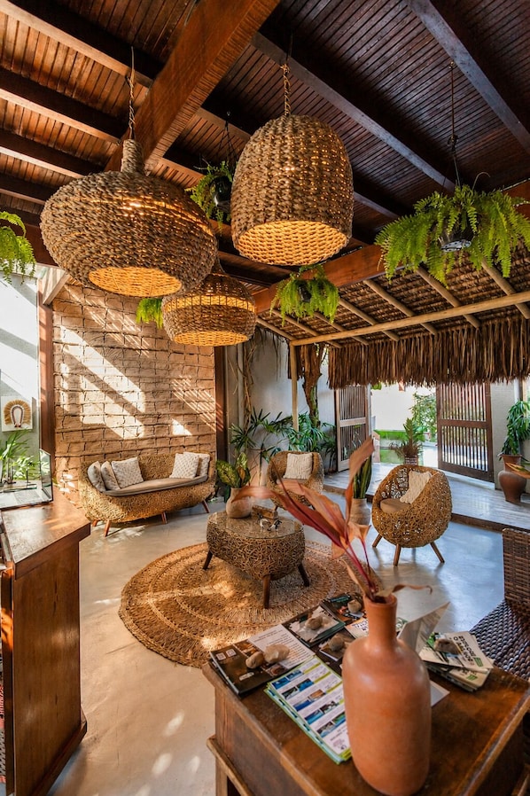 Una habitación con lámparas colgantes tejidas, muebles de mimbre, una pared de piedra y un techo de paja.