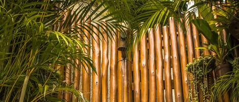 A bamboo fence with a showerhead and hanging plants.