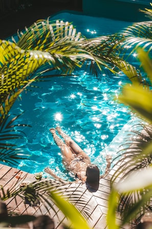 A person swimming in a clear blue pool surrounded by palm leaves. - Pousada Agua de Coco (Porto Seguro)
