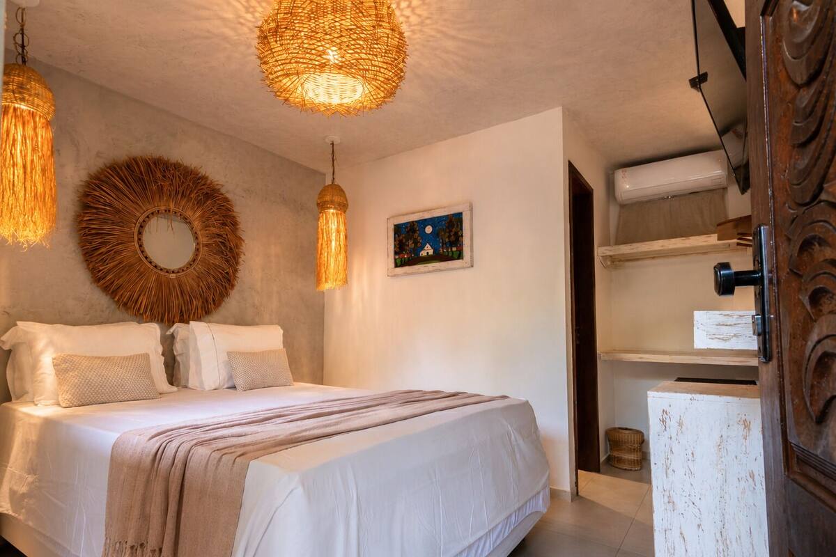 A bedroom with a bed, two hanging light fixtures, a wall-mounted mirror, and a painting.